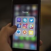 Une personne tient un téléphone intelligent. On peut voir entre autres les applications Facebook, Instagram, Messenger et Snapchat.