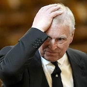 Le prince Andrew, une main sur la t&ecirc;te, regarde vers la droite.
