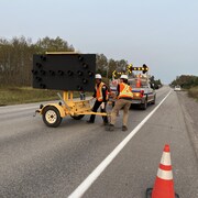 Des travailleurs installent des panneau pour fermer la route 172.