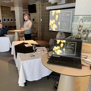 Une personne fait une présentation devant une affiche qui indique les festivités prévues pour le 30e anniversaire de la Salle Jean-Marc Dion.