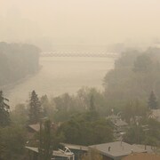 Une épaisse fumée enveloppe une forêt et une partie de la ville de Calgary, dont ce secteur de la rivière Bow enjambé par un pont difficilement visible, le mardi 16 mai 2023.