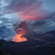 Un panache de fumée rougi par les flammes s'élève d'un feu de forêt près d'une rivière, entre des montagnes, dans le parc national Jasper, au début de septembre 2022.