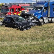 Des pompiers de l'agglomération de Longueuil s'activent sur la scène d'un accident impliquant un véhicule complètement écrasé entre un véhicule lourd et une voiture accidentée, sur le bord d'une autoroute.