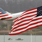 Un avion s'envole au-dessus du fleuve, devant un drapeau américain.