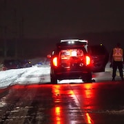 Deux policiers se tiennent à côté d'une voiture, tandis que deux autres véhicules sont sortis de route.