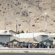 Une file d'hommes, de femmes et d'enfants devant des hangars