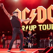 Le chanteur Brian Johnson saluant la foule les bras ouverts.