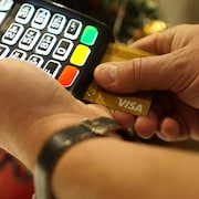 Des mains manipulent un terminal de carte de crédit pour une transaction avec une carte Visa