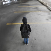 Un enfant portant un sac à dos seul dans un stationnement.