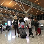 Des voyageurs valises à la main marchent dans le terminal international de l'aéroport de Calgary. 