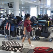 Un passager cherche ses son bagage parmi une pile de valises et de sacs non réclamés à l'aéroport Pierre Elliott Trudeau, à Montréal. 
