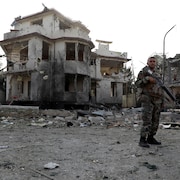 Un soldat devant un édifice en ruines. 