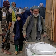 A Taliban fighter stands guard as people receive food rations distributed by a South Korean humanitarian aid group, in Kabul, Afghanistan, on May 10. World Vision says it was forced to cancel a recent food shipment to the Taliban-run country because of a Canadian law banning dealings with terrorists. (Ebrahim Noroozi/The Associated Press)