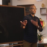 Le rappeur Webster (Aly Ndiaye) est devant un tableau dans une classe. 