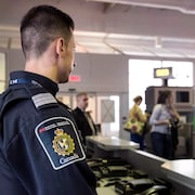 Un agent frontalier du Canada observe les passagers à une porte d'embarquement dans un aéroport