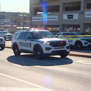 Deux véhicules de police et deux véhicules des services d'urgence près d'un stationnement et d'un cordon jaune de scène de crime.