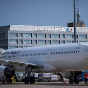 Un avion sur lequel on peut lire « Air France » est posé au sol près d'un bâtiment sur lequel il est aussi inscrit « Air France ».