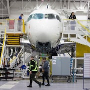 Des employés s'affairent sur un avion en construction dans une usine aéronautique.
