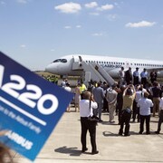 Des membres des médias prennent des images d'un avion A220 sur un tarmac.