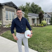 Un homme, avec un casque de construction à la main, debout devant une rangée de maisons.