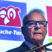 Gros plan d'Alain Bouchard devant le logo de Couche-Tard.