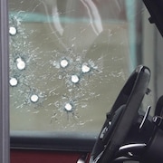 La vitre d'un véhicule fracassée par des impacts de balles, vue de l'intérieur.
