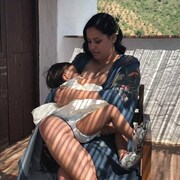 Une mère autochtone allaite son bébé sur un balcon à l'extérieur.