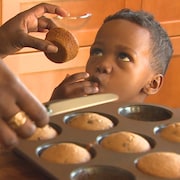 Un jeune garçon se lèche les doigts tandis que sa mère lui tend un muffin sorti du four.