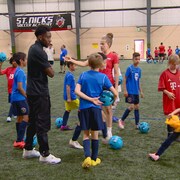 Alphonso Davies sur un terrain de soccer avec des enfants et des entraîneurs. 