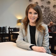 Amanda Simard, assise à une table dans un café, sourit à la caméra.