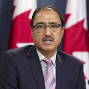 Une personne parle devant des drapeaux canadiens.