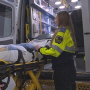 Deux ambulanciers préparent une civière devant la porte arrière d'une ambulance.