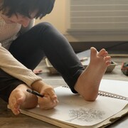 Amélie Archer, atteinte de paralysie cérébrale, dessine, un crayon à la main.