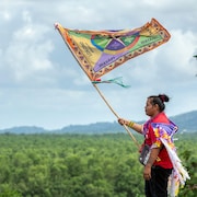 Une personne tient un drapeau devant une forêt tropicale.