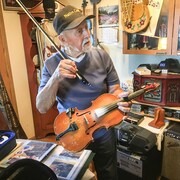Angus Beaulieu qui tient son violon, entouré d'instruments et autres souvenirs, chez lui, à Fort Resolution, dans les Territoires du Nord-Ouest, en juin 2021. 