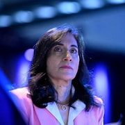 Anita Anand regarde au loin, baignée de lumière bleue dans une salle de conférence.