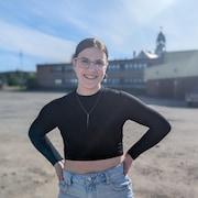 Une jeune femme sourit pour la photo devant une école secondaire.