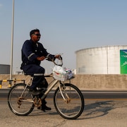 Un employé en bleu de travail se déplace à bicyclette non loin d'un réservoir de pétrole.