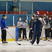 Des patineurs portant des chandails d'arbitres sont sur la glace d'une aréna.            
