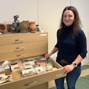 Vanessa Morin ouvre un tiroir qui dévoile un ensemble de découvertes archéologiques. Il semble contenir des roches et des pointes parmi d'autres artefacts. 