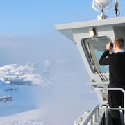 Un membre d'un navire d'inspection danois observe avec des jumelles au loin.