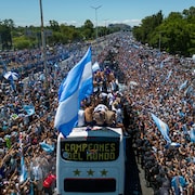 En Argentine, un autobus avec des hommes sur le toit roule au milieu d'une foule en liesse.