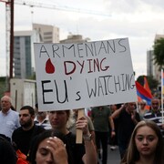 Des gens tiennent des drapeaux de l'Arménie et une pancarte sur laquelle est écrit : des Arméniens meurent tandis que l'UE regarde.