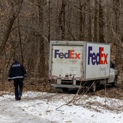 Un policier du SPVQ se dirige vers un camion FedEx immobilisé dans un sous-bois.