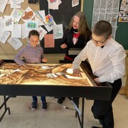 Trois élèves font de dessins sur la table lumineuse d'art de sable. 