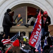 Des partisans de Donald Trump, dont certains portent des drapeaux américains ou pro-Trump, grimpent dans le Capitole à travers une fenêtre qu'ils ont cassée.