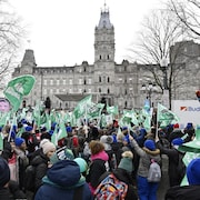 Des manifestants sont massés devant l'Assemblée nationale et brandissent pancartes et banderoles.