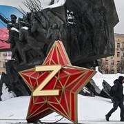 Deux personnes marchent devant un monument honorant l'armée russe, qui comprend un drapeau de la Russie et une étoile marquée du Z qui symbolise le soutient à l'armée.