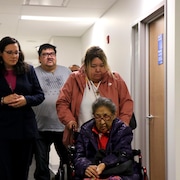 Trois personnes marchent en accompagnant une femme âgée en fauteuil roulant. 