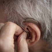 Un homme âgé place une prothèse auditive dans son oreille.